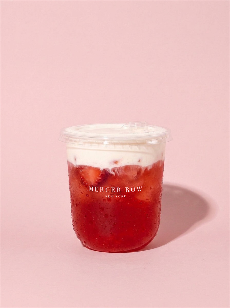 STRAWBERRIES AND CREAM, a red strawberry drink under a white cream cap, in a cup printed with the Mercer Row logo